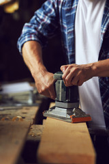 Carpenter using electric sander on wooden board in his workshop