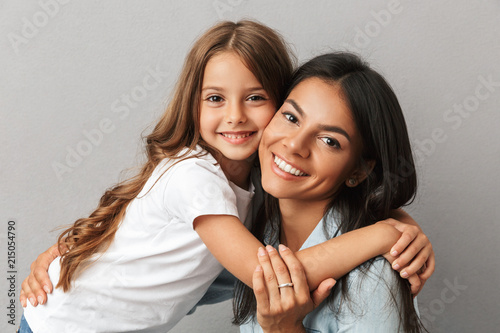 Photo of attractive woman with little daughter smiling and hugging together, isolated over gray background Photo of attractive woman with little daughter smiling and hugging together, isolated over gray background