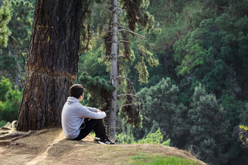Hombre sentado en la cima de una montaña contemplando el bosque que lo rodea en calma 