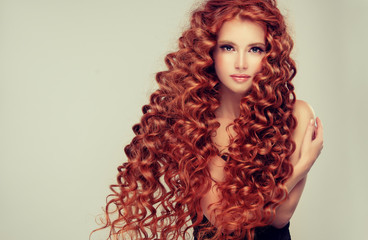 Beautiful model girl with long red curly hair .Red head . Care and beauty hair products 
