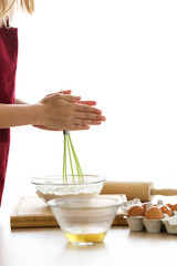 Young woman whisking eggs in glass bowl on kitchen table at home.