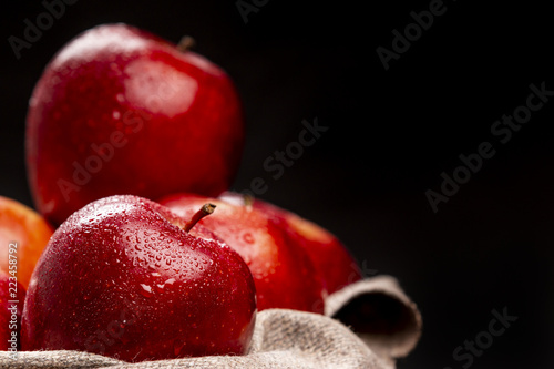 Bunch of wet red apples lying in braided bowl on black background © aitormmfoto