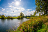 Landschaft im Sommer mit Fluss, Bäumen und Wiesen bei strahlendem Sonnenschein