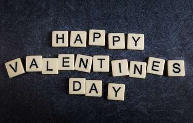Scrabble letter tiles on black slate background spelling happy valentines day
