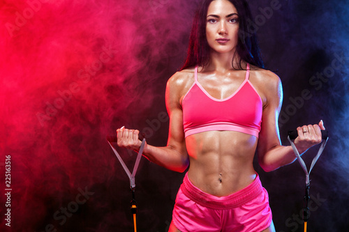 Muscular young fit sports woman athlete. Workout with bands or expander in gym on black background. Copy space for fitness nutrition ads. © Mike Orlov