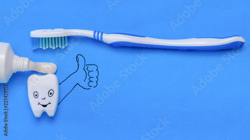 Tooth figurine with funny face and hand shows the class of toothpaste and brush. The view from the top. Flat lay. © kvladimirv