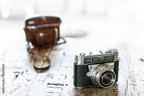 Schöne vintage Kamera im Vordergrund steht auf Holztisch mit eingeschnitzen Initialen und Namen der Hintergrund verläuft ins helle nach draußen © Petra
