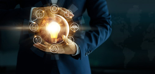 Businessman' s hand holding glowing light bulb with energy sources icon. Campaigning for ecological friendly and sustainable environment.  Elements of this image furnished by NASA