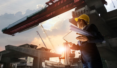 Construction engineer manager supervising progress of BTS Station Construction Project and tablet with blueprint in hands. Cranes in sunset background. Industrial technology 4.0