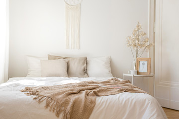 King size bed with white bedding, beige pillows and blanket next to bedside table with flower, coffee bug and print in frame, real photo