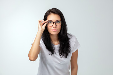 Shocked pretty woman touching her glasses and looking at the camera, surprised female staring at the camera isolated on the white background.