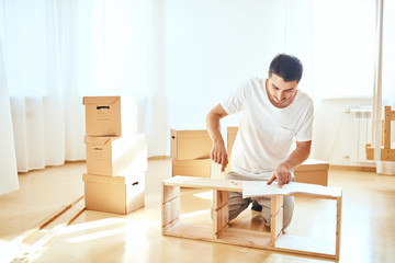 Concentrated young man reading instructions to assemble furniture at home