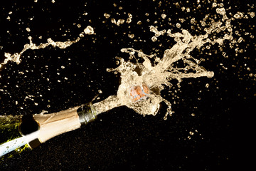 Celebration theme with explosion of splashing champagne sparkling wine on black background.