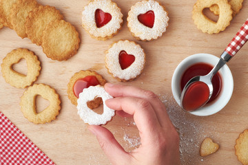 Traditional Christmas Linzer cookies with strawberry jam in wooden tray on dark background