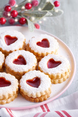 Traditional Christmas Linzer cookies filled with strawberry jam on light table with Xmas decorations