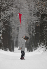 child girl looks at on santa claus hat in the forest