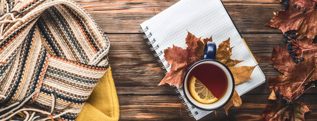Autumn fashion seasonal concept yellow warm soft sweater Scandinavian knitted scarf cup hot black tea coffee Fall fallen maple leaves on wooden table with notebook pen. Flat lay Top view vintage style