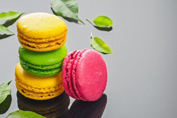 Colorful various French sweet macaroons dessert cake macarons on dark gray background decorated with green leaves copy space