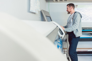 Mann arbeitet am Großformatdrucker in Werbemittelherstellung 