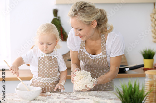 Plakat Mała dziewczynka i jej blondynki mama w beżowych fartuchach bawić się i śmia się podczas gdy ugniatający ciasto w kuchni. Domowe ciasta na chleb, pizzę lub upiecz ciasteczka. Rodzinna zabawa i gotowanie koncepcji