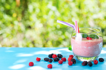 Glass of berry smoothie with straw and berries on blue table