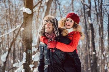 Man carrying his woman piggyback on a winter day in a joyful manner, they have fun in this season 