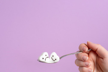 spoon with a piece of sugar in a female hand on a lilac background.