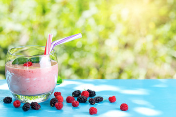 Glass of berry smoothie with berries under bright sun