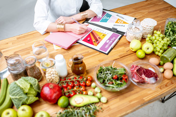 Dietitian writing diet plan, view from above on the table with different healthy products and drawings on the topic of healthy eating