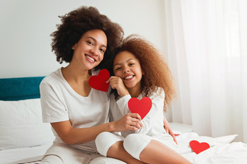 Mother and daughter enjoying on the bed, holding red hearts 