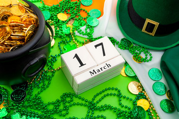 The luck of the Irish meme and Happy St Patricks day concept theme with a calendar, leprechaun hat, beads necklace and pot of gold coins on the Ireland flag isolated on green background