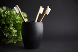 Three bamboo toothbrushes in a black glass with copy space on a dark background
