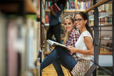 Two female students read and learns by the book shelf at the library.Reading a book.