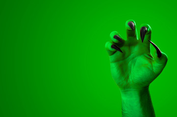 Halloween, nightmare creature and evil monster horror story concept with a scary zombie or demon hand with creepy long black nails isolated on green with a clip path cutout and copy space