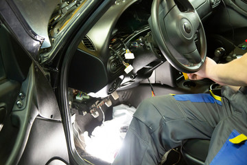 Electrician works with electric block in car. Close-up of automobile inside under raised hood. Service man hands working with cables of auto .