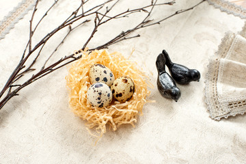 Easter quail eggs in a nest and branches of willow on a light background