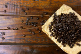 roasted coffee beans on paper on rustic wooden table, beans around scattered