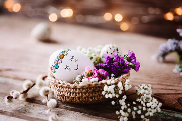 Kleines baby Osterei liegt im Osternest dekoriert mit Frühlingsblumen und Lichterbokeh