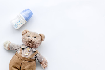 Feed baby concept. Teddy bear toy near small bottle with food on white background top view copy space