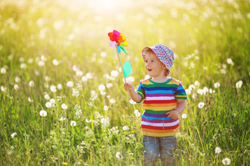 Baby boy standing in grass on the fieald with dandelions