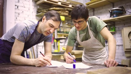 Two carpenters discuss drawing (round wood) in the workshop