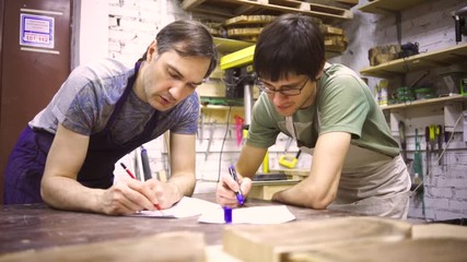Two carpenters discuss drawing (round wood) in the workshop
