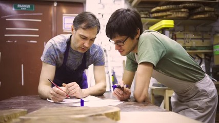 Two carpenters discuss drawing (round wood) in the workshop