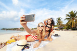 Beautiful happy girlfriends having fun on the beach taking selfies during vacation and travel
