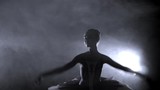 Young girl ballerina dancing and jumping in a dark, smoky room with a spotlight in the background