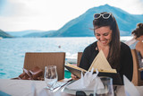 young pretty woman sitting in restaurant at seaside with mountains on background