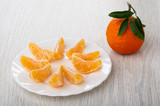 Tangerine with leaves, slices of tangerine in plate on table