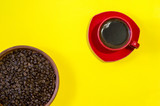 Red mug of freshly brewed coffee with roasted beans in a ceramic clay pan on a yellow background