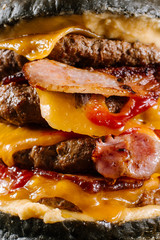 A very big black burger with three cutlets on the black background