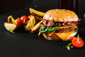 A burger with french fries, tomatoe sauce and glass of juice on the black background